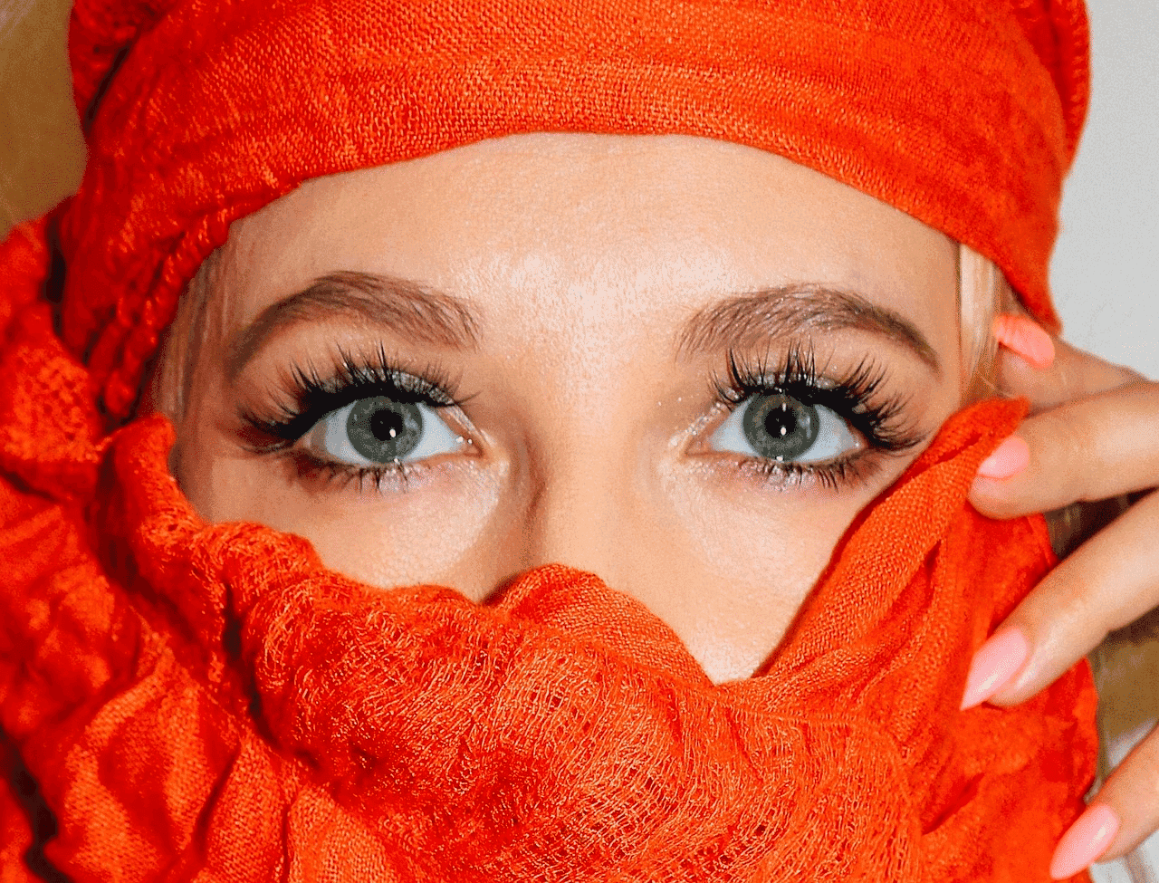 Woman's eyes with dramatic lashes, covered in vibrant orange fabric.