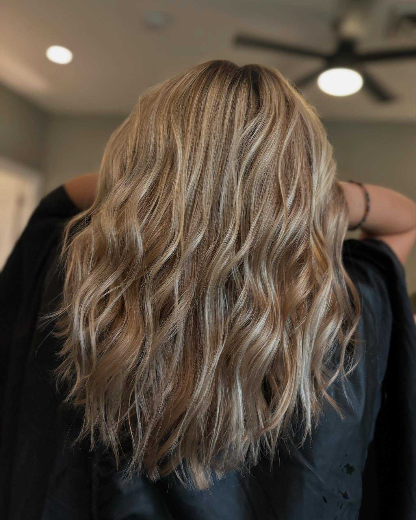 Long, wavy blonde hair from the back, under a ceiling fan indoors.